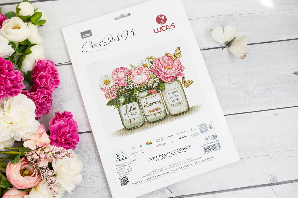 Portada del kit de punto de cruz Luca-S B7065 Little by Little Blooming sobre mesa blanca con flores