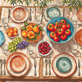 Kit de punto de cruz AVA Stitch P139 Mediterranean Table con mesa mediterránea, platos, copas, tomates, naranjas, uvas y cerezas bordados sobre Aida blanca.