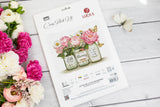 Portada del kit de punto de cruz Luca-S B7065 Little by Little Blooming sobre mesa blanca con flores