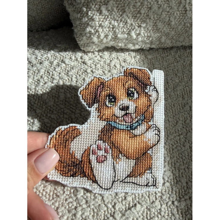 Kit de punto de cruz Andriana SANZ-77 Bookmark Friend con perrito marrón y blanco de ojos grandes, collar azul y diseño para marcapáginas sobre canvas plástico blanco.